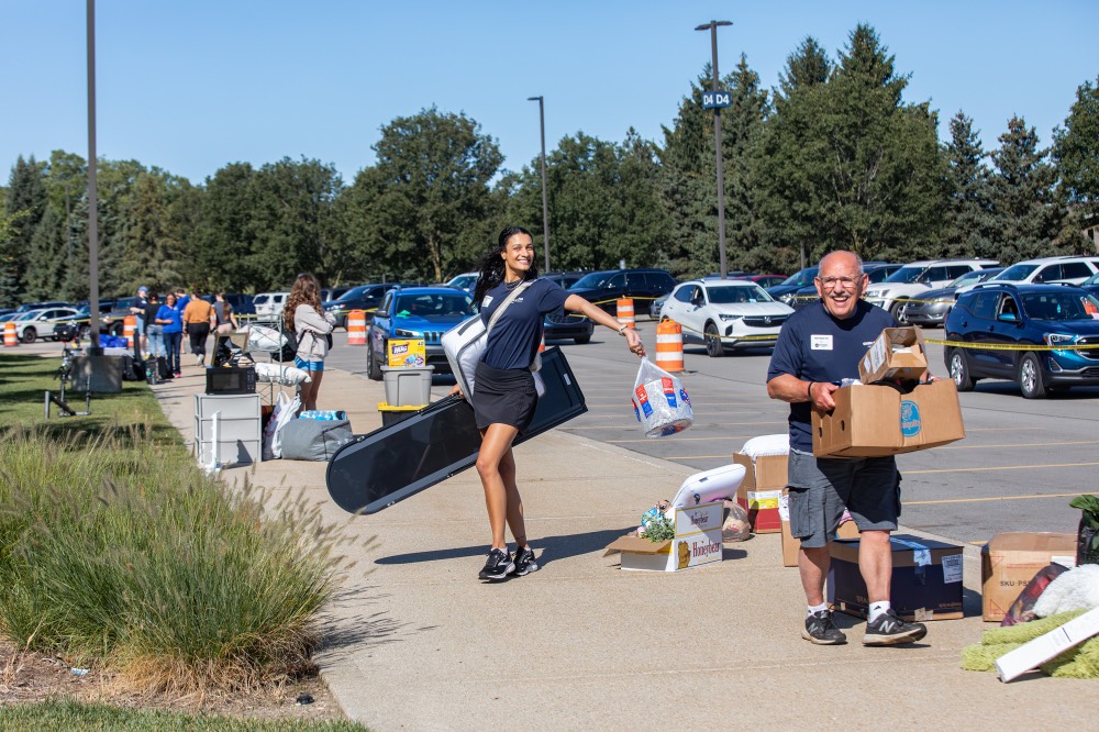 GVSU Alumna poses and GVSU Alumnus carries cardboard box